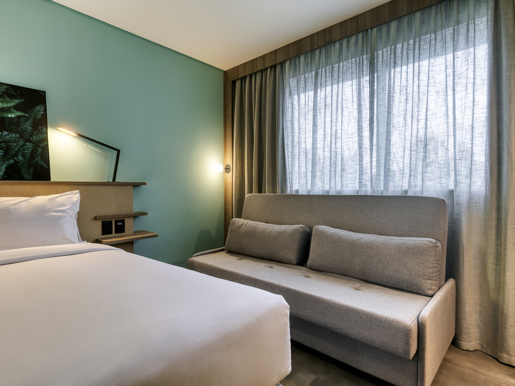 Habitación en Novotel BH Savassi con cama, sofá y pared en tono verde azulado